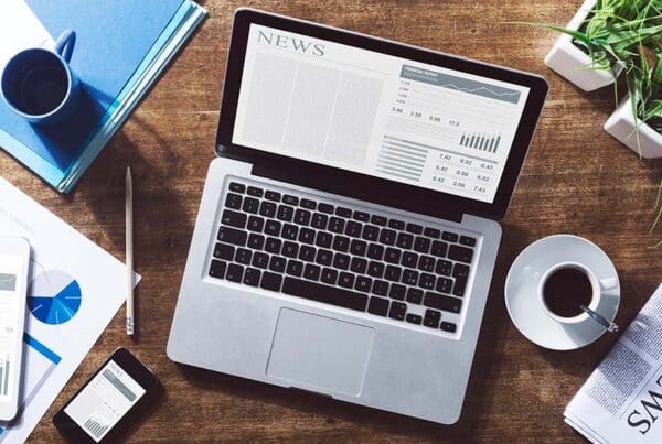 Magenta Blog Sample Post - View of a Laptop with the News Sitting on Top of a Wooden Desk Next to a Cup of Coffee and Paperwork